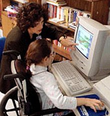 Giovane con disabilità al computer, insieme a un'assistente