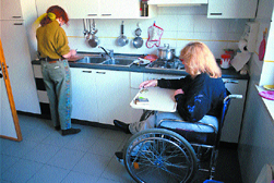 Donna in carrozzina in cucina assieme a un'assistente