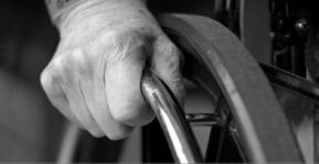 Particolare di mano di persona con disabilità che stringe la ruota di una carrozzina