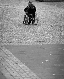 Foto in bianco e nero dell'angolo di una piazza, con una persona in carrozzina sullo sfondo