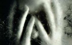 Immagine sfuocata, dietro a un vetro, di persona con le mani sulla faccia