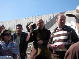 Dietro Hamdan e i turisti alternativi si vede il muro che separa Israele e la Cisgiordania