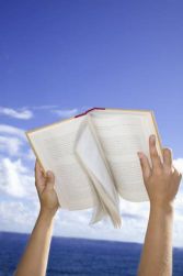 Due braccia sorreggono un libro aperto. Sullo sfondo il cielo azzurro