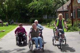 Persone con varie disabilità e diversi ausili sul viale di un parco